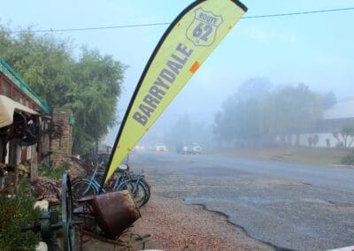 Rainy weather image of the R62 road and a yellow flag with the text Barrydale on it